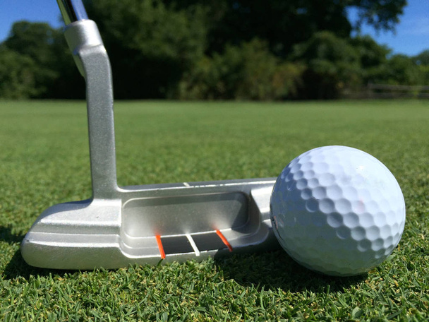 Auf dem grünen Rasen eines Golfplatzes reihen sich weißer Golfball und eiserner Putter aneinander. zielen und in das Loch stecken. - Foto, Bild