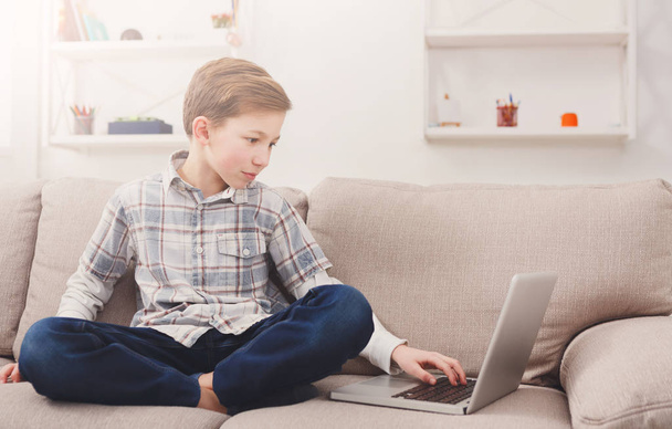 Bambino ragazzo utilizzando il computer portatile sul divano a casa
 - Foto, immagini