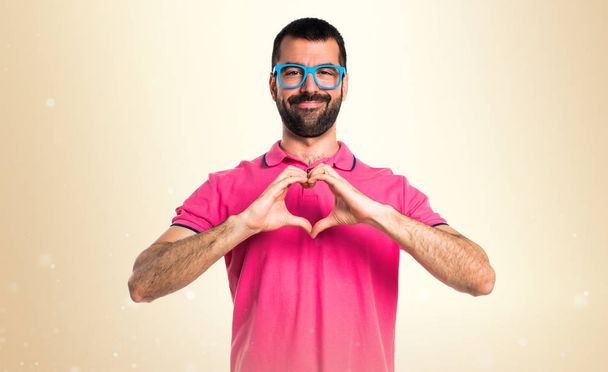 Человек в разноцветной одежде делает сердце с руками на охре
 - Фото, изображение