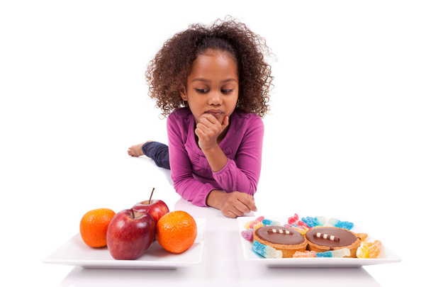 Little African Asian girl hesitating between fruits or candy - Foto, Imagem