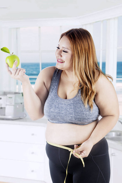 Obese woman holds apple in kitchen - Zdjęcie, obraz