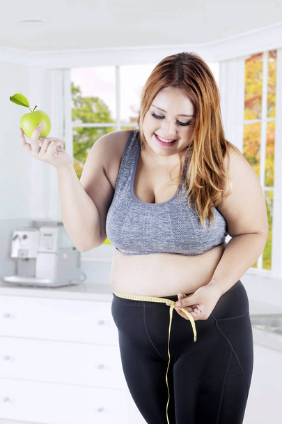 Obese woman measuring stomach in kitchen - Foto, Bild