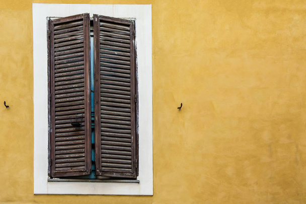 Fenêtre en bois avec volets fermés sur un vieux mur peint en jaune d'une maison italienne
 - Photo, image