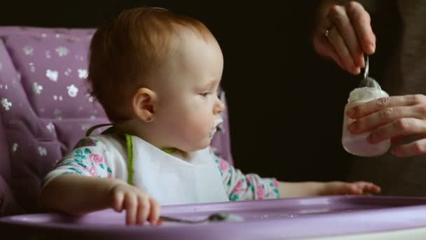 χαριτωμένο μωρό κάθεται σε ένα καρεκλάκι ενώ σιτίζονται σε γκρι φόντο - Πλάνα, βίντεο