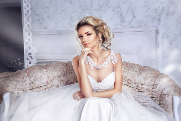 Beautiful bride posing in wedding dress sitting on sofa in a white photo Studio. - Photo, image