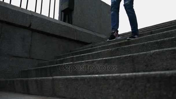 Zbliżenie na kobiece nogi w niebieskie jeansy i czarne trampki działa w dół po schodach - Materiał filmowy, wideo