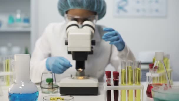 Medical scientist viewing samples of microorganisms on microscope at laboratory - Felvétel, videó