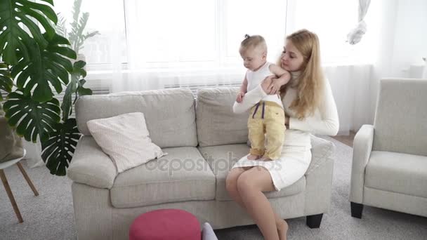 Mother dressing her small baby boy at home on the sofa - Materiał filmowy, wideo
