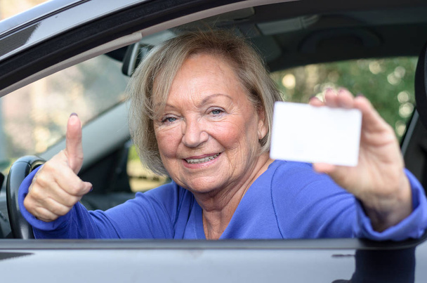 Mujer mayor apoyada en un coche que muestra su licencia
 - Foto, Imagen