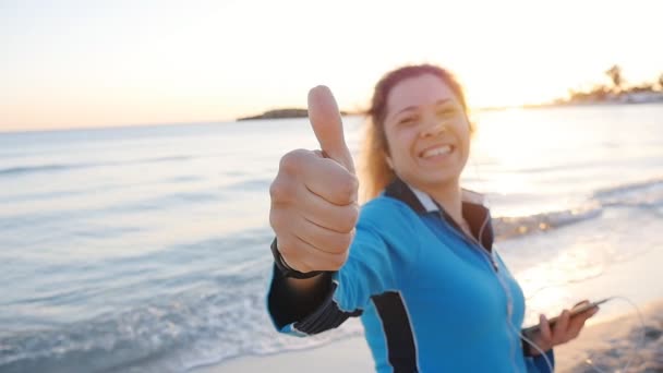 Jovem mulher dando polegares para cima sinal de mão na praia
 - Filmagem, Vídeo