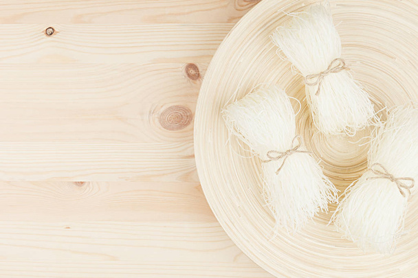 Sheaf raw asian cellophane noodles on plate on beige wooden board with copy space, top view. - Фото, зображення