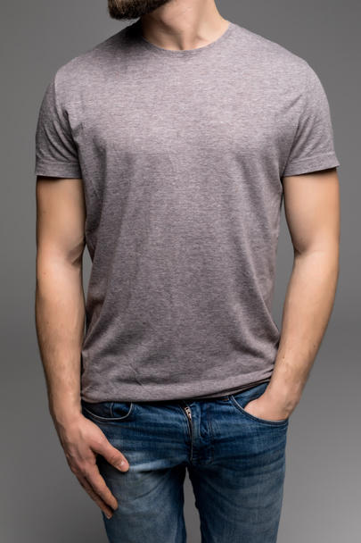 A man in a grey t-shirt and denims holds his hands in pockets. - Foto, imagen