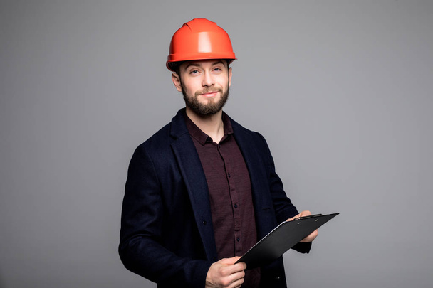 Adult Caucasian man in a black suit and construction helmet holding black folder - Photo, Image