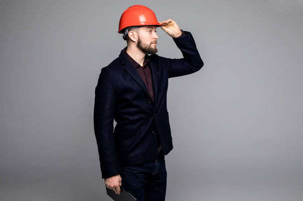 Homem de terno preto e capacete de construção olhando para o lado e segurando pasta preta
 - Foto, Imagem