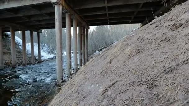 Camera moves from right to left and removes the river flowing under the bridge in the early spring. - Video