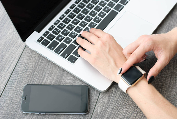 Female hand with smartwatch with holding mobile phone on laptop computer - Fotó, kép