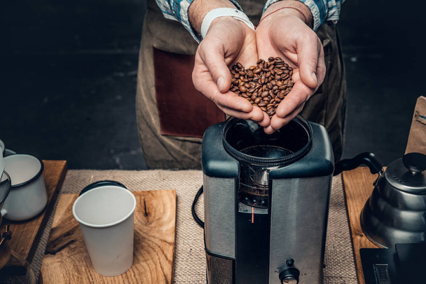 Mies laittaa kahvipapuja kahvinkeittimeen
 - Valokuva, kuva