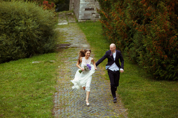 Smiling wedding couple run along the park  - Photo, Image