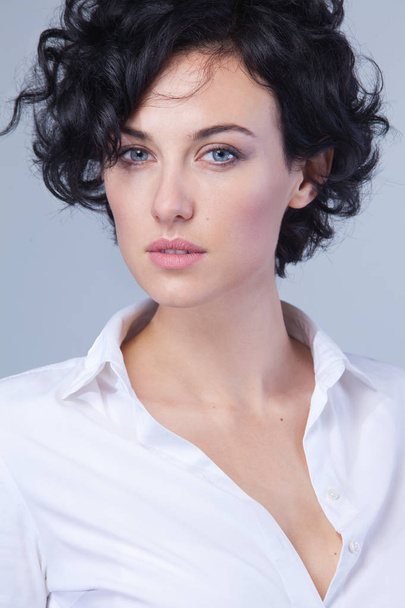 Close up portrait of fashionable successful female with short curly hairstyle wearing white trendy shirt, looking at the camera. - 写真・画像