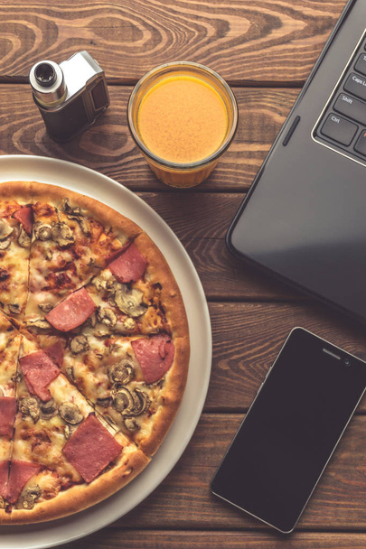 Pizza met ham en paddestoelen op een plaat, laptop, elektronische sigaret of vape - Foto, afbeelding