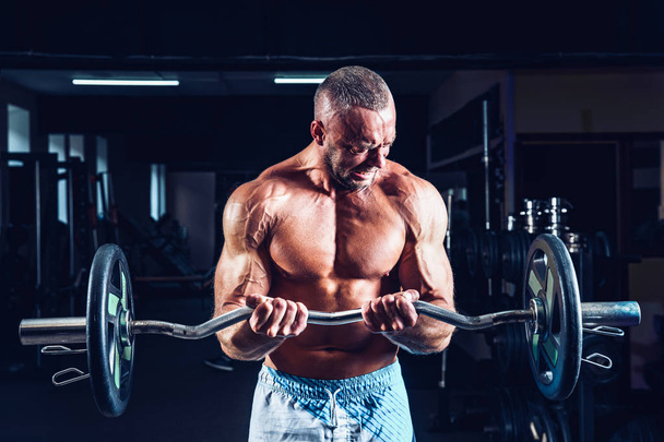 Muscular bodybuilder guy doing exercises on biceps with big dumbbell in gym - Foto, Imagen