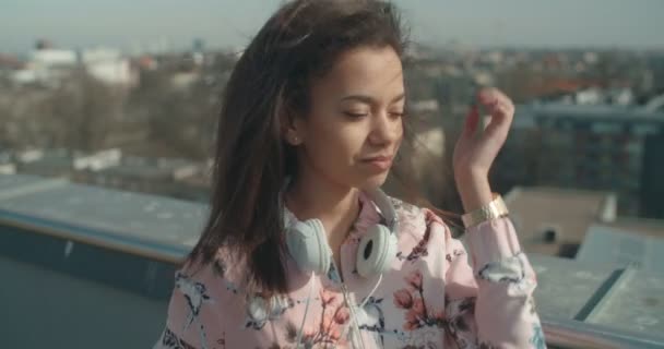 Young woman with headphones enjoying time on a rooftop. - Materiaali, video