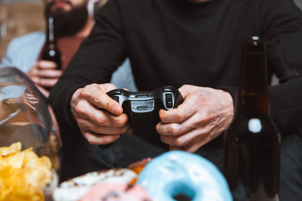 men with a beard sitting on the couch at home with beer and joysticks in the hands of playing computer video games - Foto, immagini