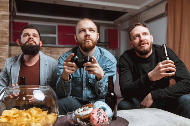 men with a beard sitting on the couch at home with beer and joysticks in the hands of playing computer video games - Fotoğraf, Görsel