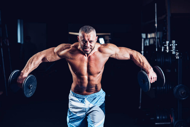 Muscular man training his shoulders with dumbbells in gym - Foto, afbeelding