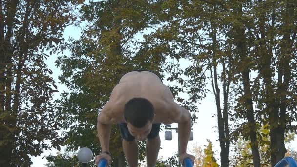 強い筋肉の男が公園で逆立ちをしています。屋外の水平バー上のスタントをやって筋肉男性フィットネス男に合います。選手のトレーニングは、筋肉の外側で逆立ちを実行します。スローモーション - 映像、動画