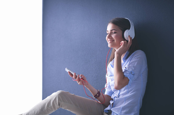 Smiling girl with headphones sitting on the floor near wall - Foto, imagen