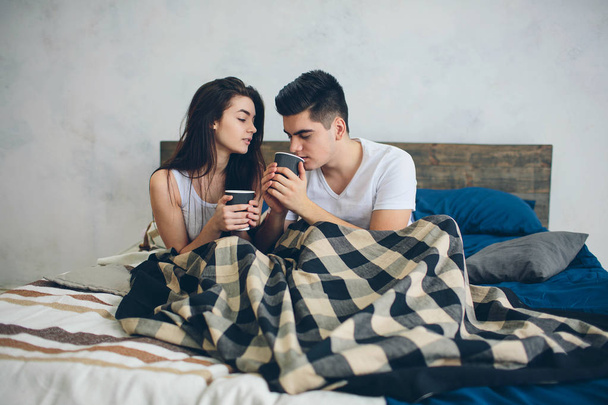 A young man and a woman are drinking coffee in the morning in bed. Romantic morning at home - Zdjęcie, obraz