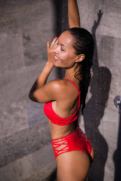 Urheilullinen nuori kaunis seksikäs nainen punaisessa uimapuvussa virkistävässä suihkussa uima-altaan jälkeen. Ulkona elämäntapa kuva kuuma aurinkoinen kesäpäivä
. - Valokuva, kuva
