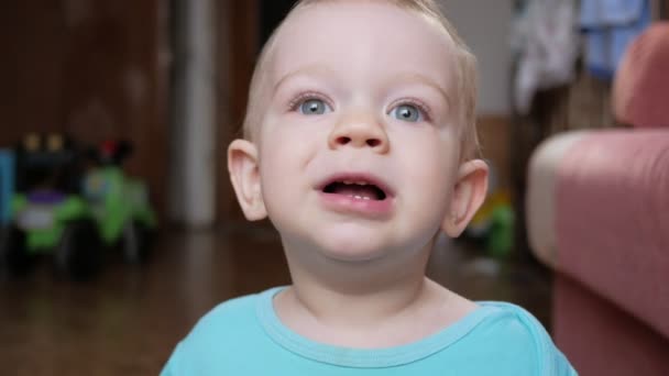 Attractive 2 year old boy looks at the camera and smiles and changes facial expressions. Home furnishings. Blue T-shirt. - Video
