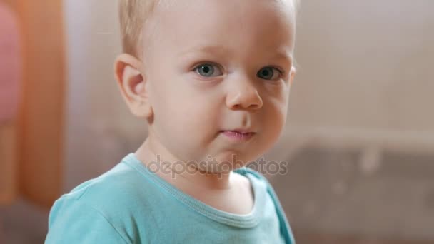 Attractive 2 year old boy looks at the camera and smiles and changes facial expressions. Home furnishings. Blue T-shirt. - Filmmaterial, Video