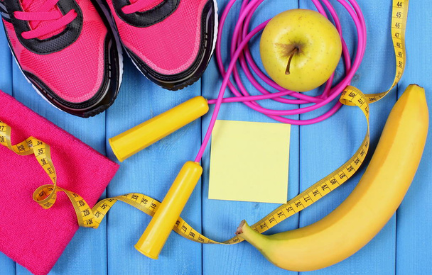 Pink sport shoes, fresh fruits and accessories for fitness on blue boards, copy space for text on sheet of paper - Foto, Bild