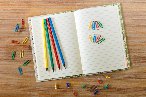 Creatieve werkplek met geopende notitie boek, potloden en kleurrijke clips .wooden table.top uitzicht. - Foto, afbeelding