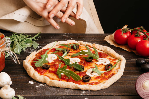 Hands cooking pizza in the kitchen. Pizza ingredients on the wooden table - Foto, Imagen