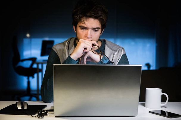Joven guapo trabajando con el ordenador portátil en su oficina por la noche
. - Foto, imagen
