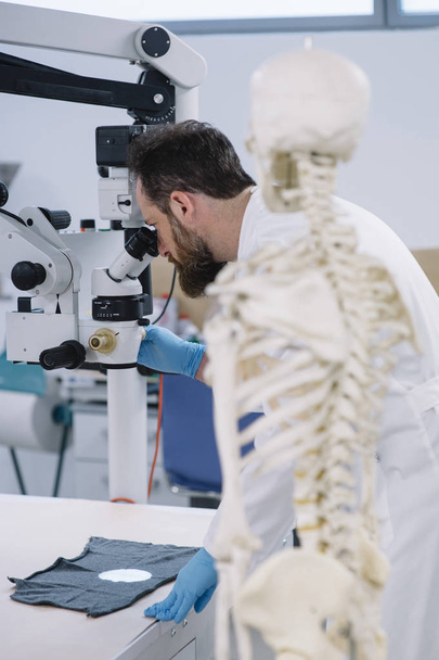 Scientist in laboratory that looks at microscope and a skeleton  - Photo, Image