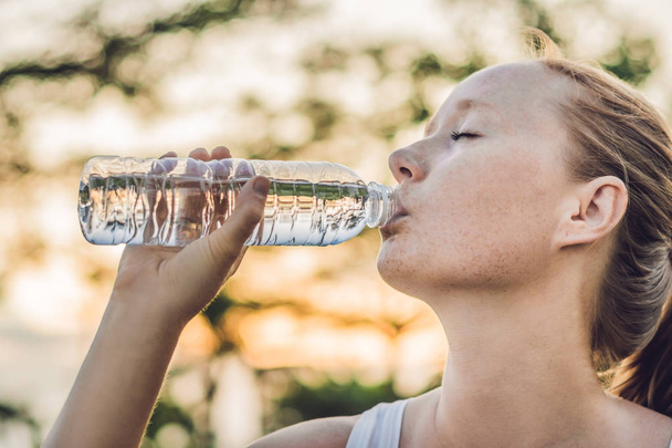 Sportliche Frau trinkt an sonnigem Tag Wasser im Freien - Foto, Bild