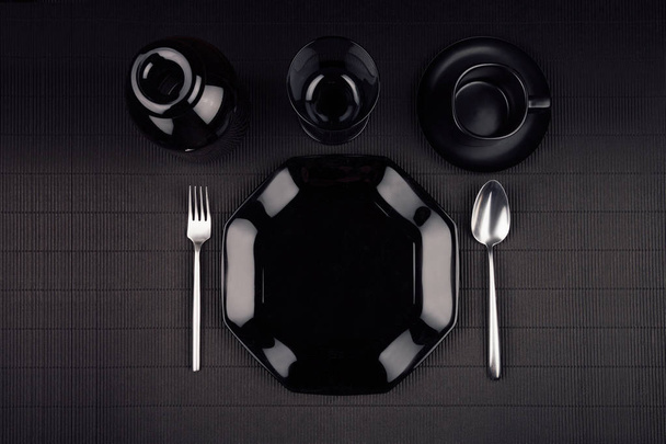 Black plate with cutlery on dark modern minimalistic mat background, top view. - 写真・画像