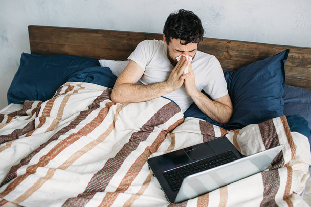Bearded man lying in morning bed with laptop - 写真・画像