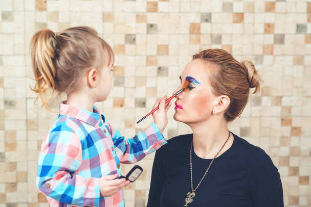Schattig klein meisje doet make-up voor haar mooie moeder. Toned. - Foto, afbeelding