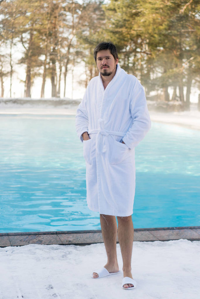 Young man in bathrobe near outdoor swimming pool at winter - Фото, изображение