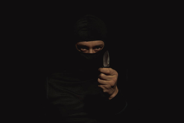 Ένας άντρας σε μια μαύρη μάσκα με ένα μαχαίρι στο χέρι του. - Φωτογραφία, εικόνα