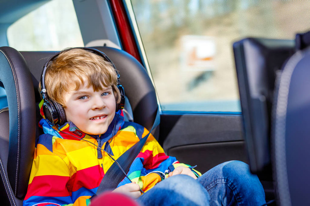 Little blond kid boy watching tv or dvd with headphones during long car drive - Photo, Image