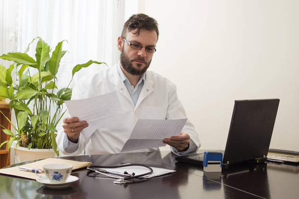 Arts in het kantoor aan een bureau zitten en lezen van medische dossiers  - Foto, afbeelding