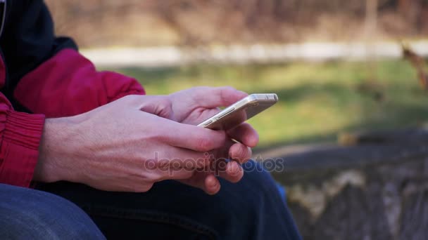 Young Man using a Mobile Phone on a Bench in the City Park - Πλάνα, βίντεο
