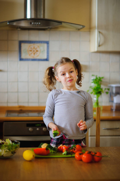 Girl 8-9 years old in the kitchen slicing vegetables for a salad. - Fotoğraf, Görsel